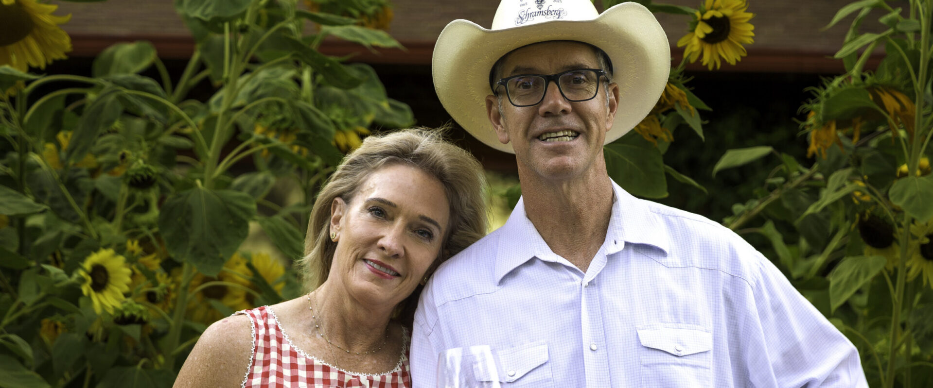 Hugh and Monique Davies toasting with wine in front of sunflowers