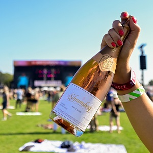 A blurry background of the main stage at Bottlerock while a hand is holding a bottle of Schramsberg Brut Rosé