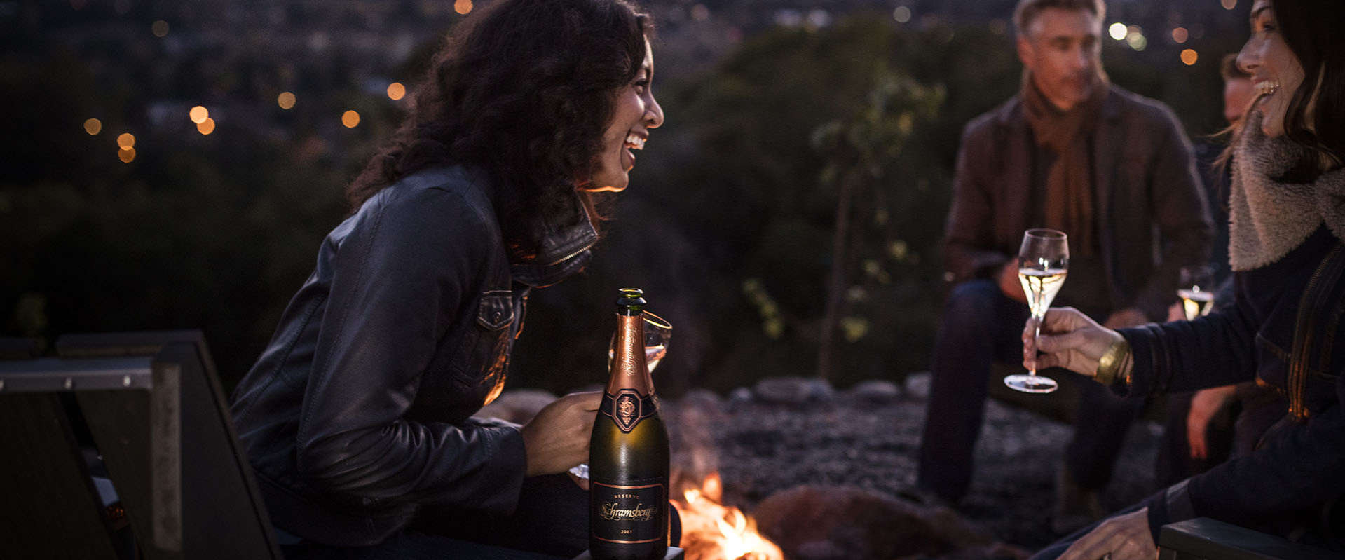 Woman laughing by a fire pit and enjoying Schramsberg sparkling wine