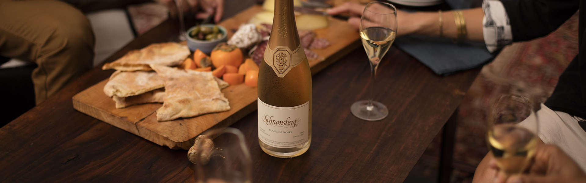 People around a coffee table enjoying Schramsberg Blancs de Noirs sparkling wine paired with a charcuterie board.