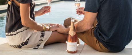Couple holding hands and enjoying Brut Rosé by a swimming pool